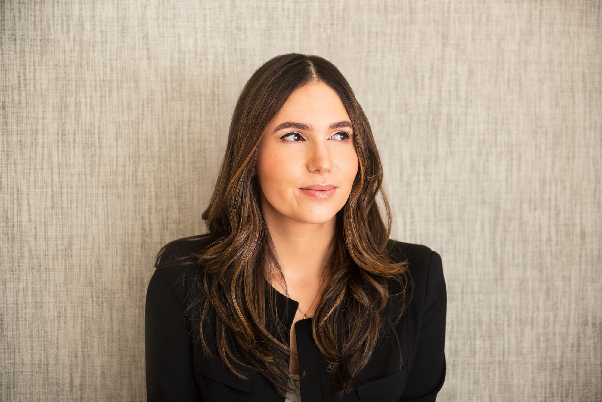 Photo of Cristina Cordova on a taupe, textured background, looking away.