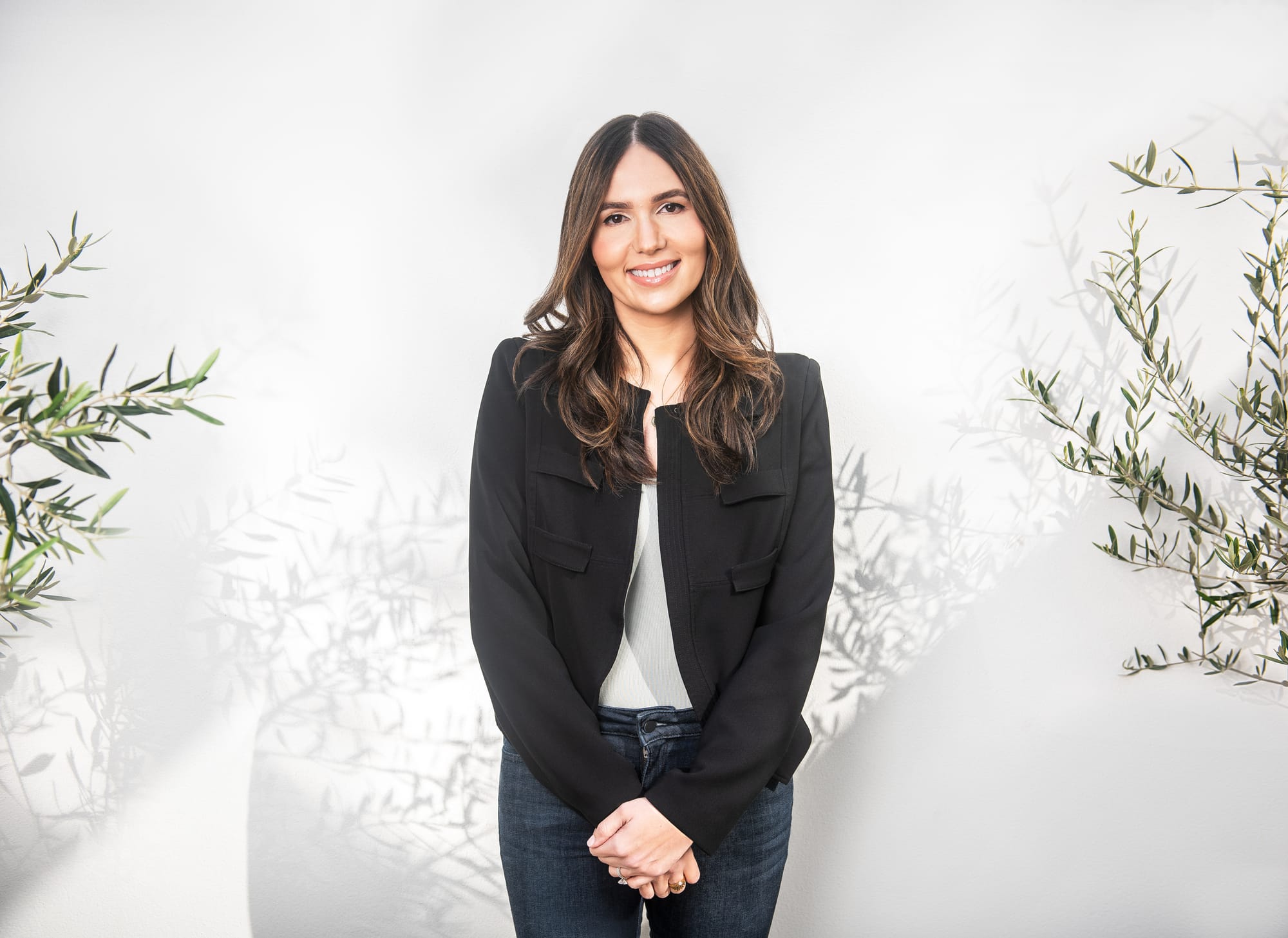 Photo of Cristina Cordova in a black jacket against a white background with olive branches.